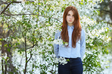 Portrait of a beautiful redhead women in shirt and jeans in blossom apple tree garden in spring time