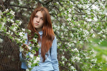 Portrait of a beautiful redhead women in shirt and jeans in blossom apple tree garden in spring time