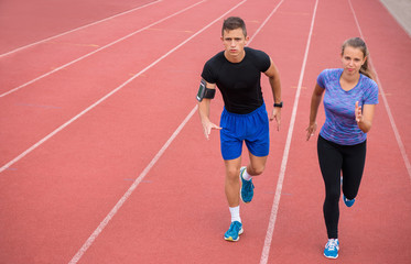 Obraz premium Two young athletic people running on race track. Male and female professional athletes running on athletics race track.