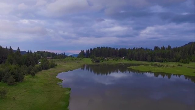 Fast flight at surface level over a lake. Beautiful clouds and forest are reflected in the water.