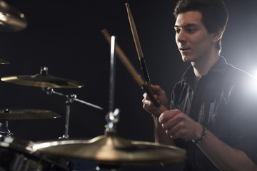 Side View Of Young Drummer Playing Drum Kit In Studio