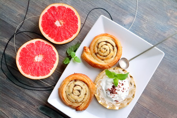 Grapefruit halves, roll cake and creamy dessert with mint leaves on a wooden table