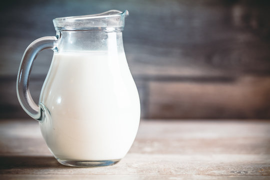 Toned photo. Color tone tuned. Fresh milk in glass jug on wooden background. Selective focus.