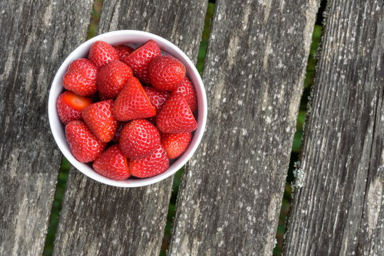 Fresh strawberries in a white bowl, on a wood deck
