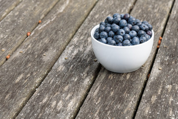 Fresh blueberries in a white bowl, on a wood deck
