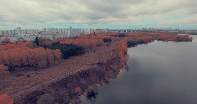 Aerial shot of golden trees on river bank during autumn season. A path or trail going along the river bank. Moscow suburbs, Strogino district, Russia.