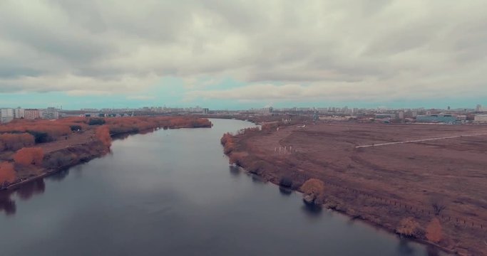Aerial shot of golden trees on river bank during autumn season. A path or trail going along the river bank. Moscow suburbs, Strogino district, Russia.