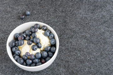 Fresh blueberries and vanilla ice cream in a white bowl, on gray background
