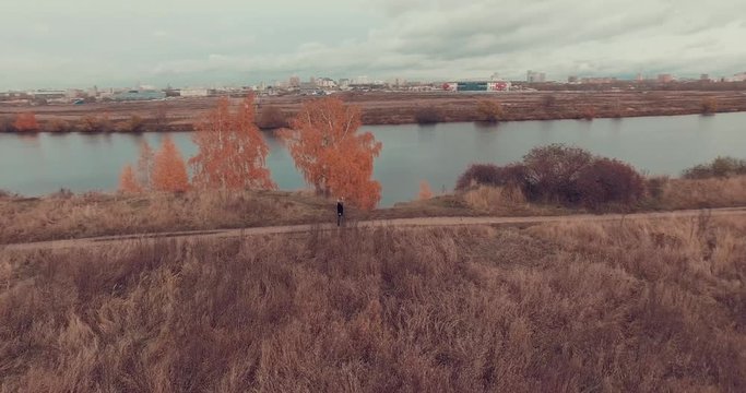 Aerial shot of golden trees on river bank during autumn season. People walking along the footpath near river bank. Moscow suburbs, Strogino district, Russia.