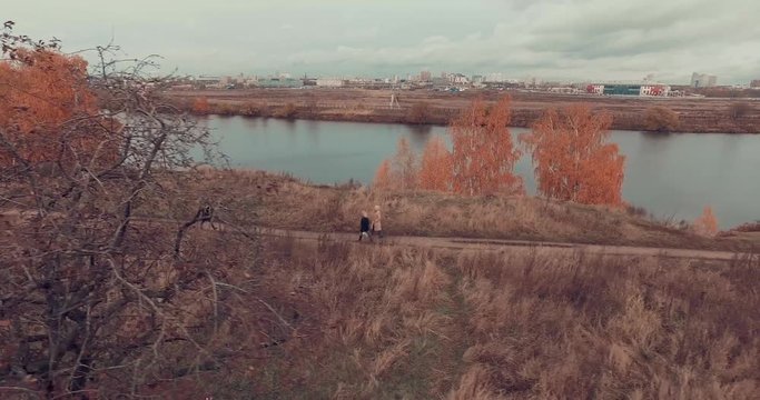 Aerial shot of golden trees on river bank during autumn season. People walking along the footpath near river bank. Moscow suburbs, Strogino district, Russia.