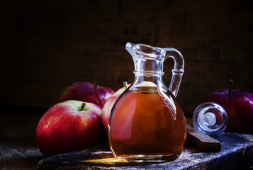 Apple cider vinegar in a glass jug, fresh apples, dark wooden ba
