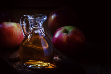 Apple cider vinegar in a glass jug, fresh apples, dark wooden ba