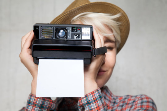Young fashion hipster smiling girl in a hat with a camera for instant photos