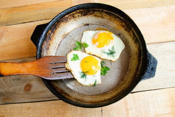 Fried eggs in a frying pan with wooden turner, wooden background