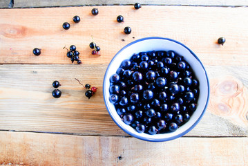 Black currant in a bowl, on an old wooden table (top view)