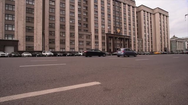 The city centre of Moscow. State Duma of the Russian Federation. The building of the state Duma of the Russian Federation with developing the flag, in front of parked cars, Past car ride.