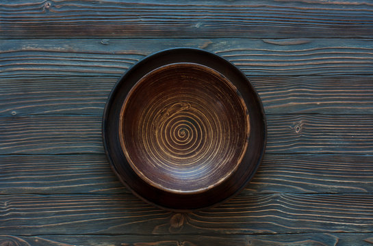 Empty clay plate over wood background, top view