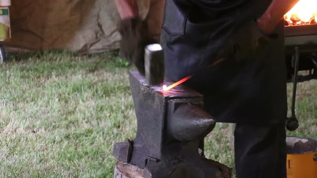 Blacksmith working on metal on anvil at forge