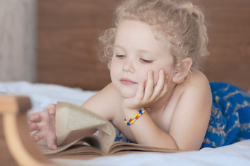 Fototapeta premium caucasian curly blonde girl reading an old vintage book with yellow sheet on a bed in the bedroom