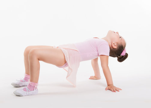 Little happy girl gymnast performs an exercise on the floor holding his leg. The girl smiles. Flexible child costume gym training.