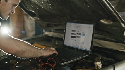 Computer diagnostics in car service: mechanic repairs the damage using the pc under the hood in car service, slider move
