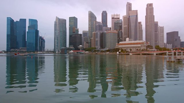 Beautiful, modern, highrise buildings of Singapore's famous skyline, stand over the Fullerton Hotel, reflected in the calm waters of the bay on an overcast day. Video UltraHD