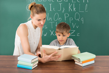 Pupil Reading With Teacher In Classroom