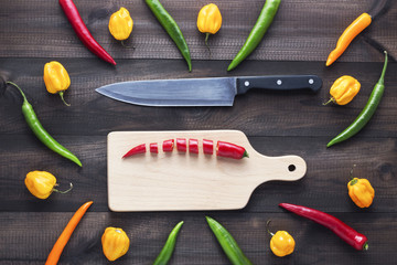 chopped cayenne chilli pepper on cutting board with knife and cayenne chilli peppers and habanero peppers on wooden table. Image with copyspace.