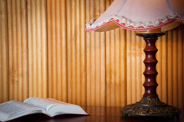 Open book on table and old vintage lamp on wooden background at home in the evening. Horizontal view. Space for text.