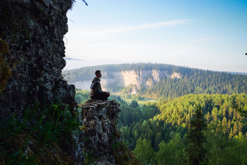 Man sitting on the top of the mountain in yoga pose, leisure in harmony with nature