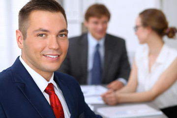 Portrait of cheerful smiling business man  against a group of business people at a meeting.