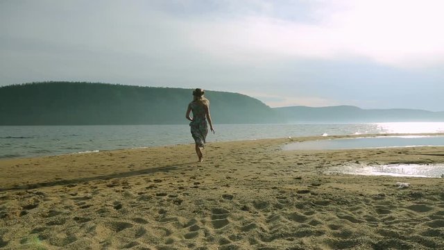 Silhouette of young women running around and jumping on the sandy beach at sunset.