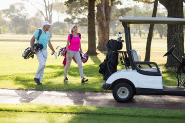 Full length of mature golfer couple by golf buggy