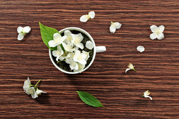 Cup of green tea leaves and jasmine flowers on wooden background