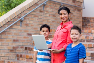 Smiling female teacher with students using laptop 