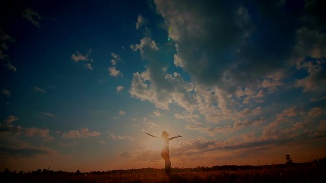 Young girl with outspread hands have fun at sunset in the field