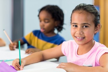Smiling schoolgirl with classmate writing on book