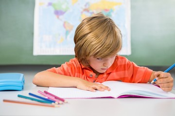 Boy writing on book in classroom