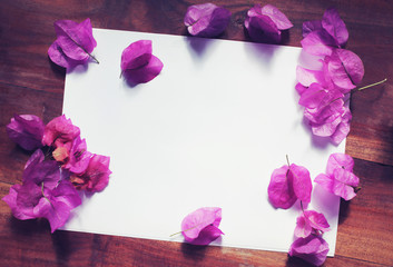 White paper pink flowers wooden desk top view