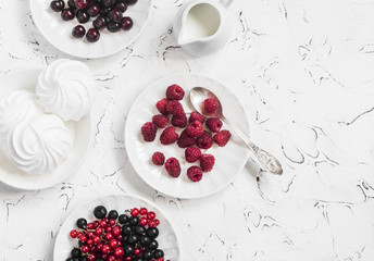 Raspberries, red and black currants, cherry, a meringue, cream on a rustic cutting board, on light background