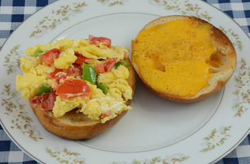 Scrambled egg bagel sandwich with chopped green bell peppers and tomatoes on plate