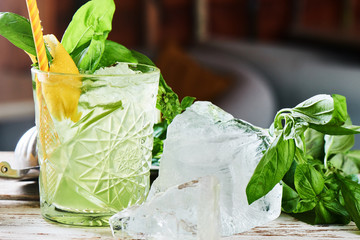 Alcoholic cocktail Basil smash in a glass beaker and a piece of ice on a wooden table