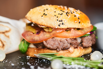 A hamburger consisting of meat patties, cheese and vegetables served on a stone Board closeup
