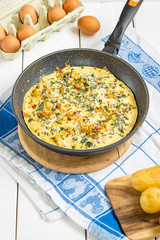 Homemade Tasty Fresh Omelette with Tomatoes, Potato, Cheese, Bacon and Herbs in a Pan on White Wooden Background, Vertical View, Close-up