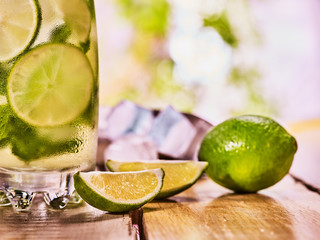 Alcohol drink. On wooden boards is part of glass with alcohol drink and ice cubes. Drink number thirty nine cocktail mohito and scoop ice and quartered lime. Country life cocktail . Light background.