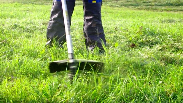 Worker mowing grass trimmer closeup