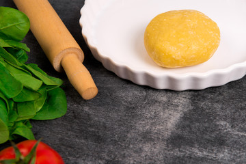 Dough, greens and tomato on grey wooden table