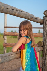 Shy, confused little girl standing near the fence in the countryside