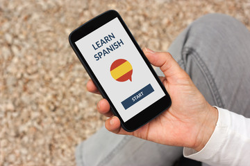 Hand holding smart phone with online learn spanish concept on screen. All screen content is designed by me
