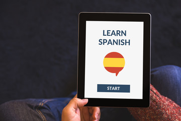 Hands holding tablet with online learn spanish concept on screen. All screen content is designed by...